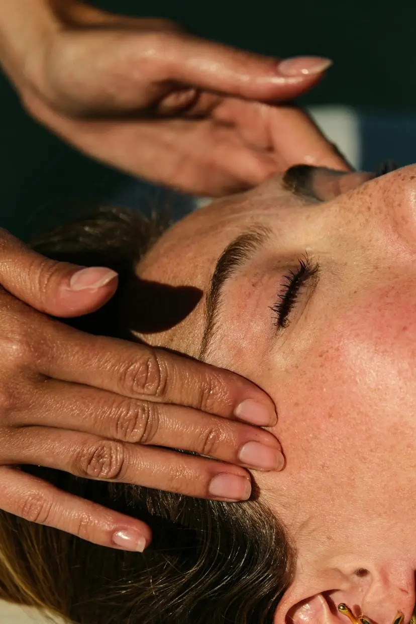 Hands massage a woman's temples during a facial treatment.